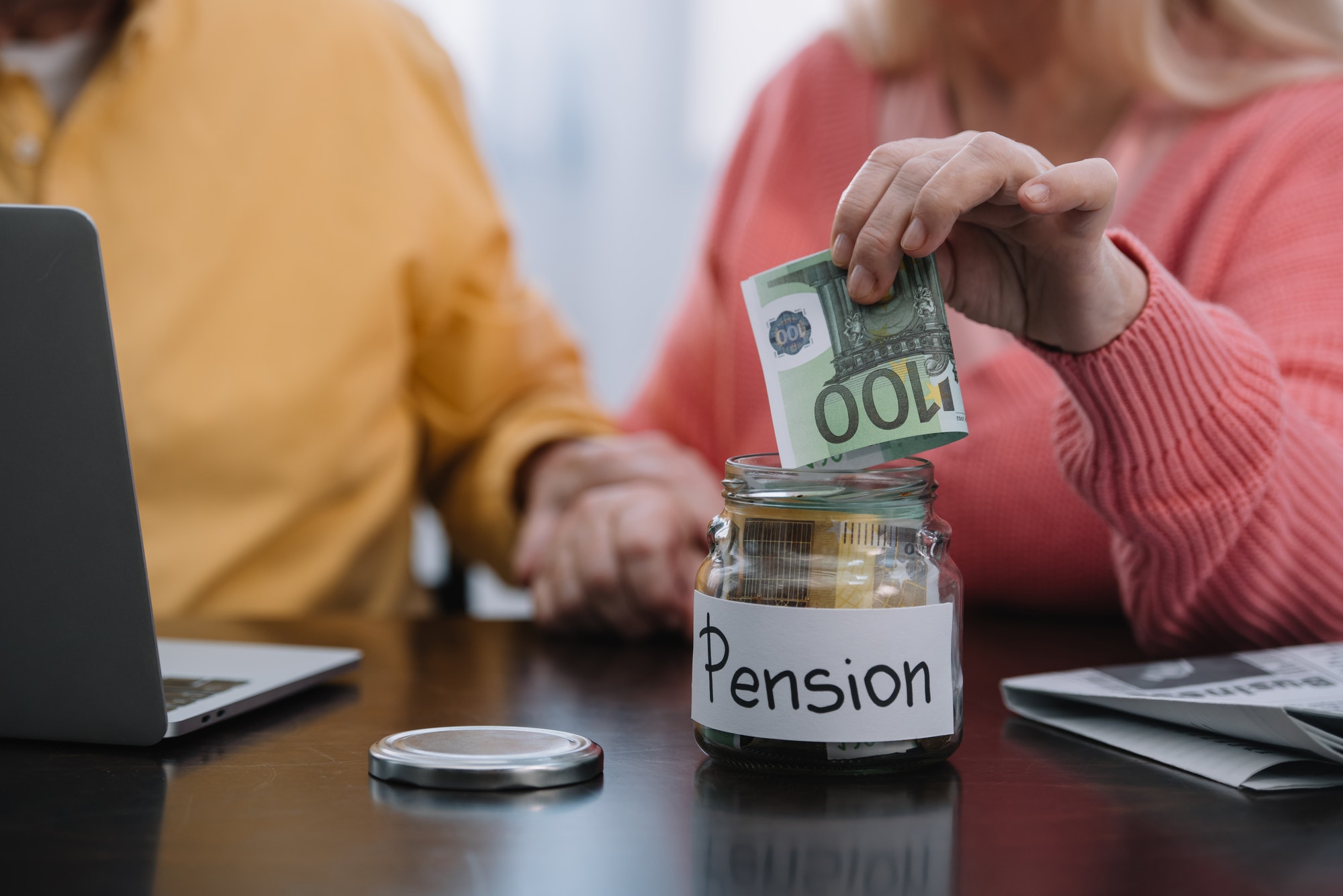 cropped view of senior couple putting money in glass jar with 'pension' word
