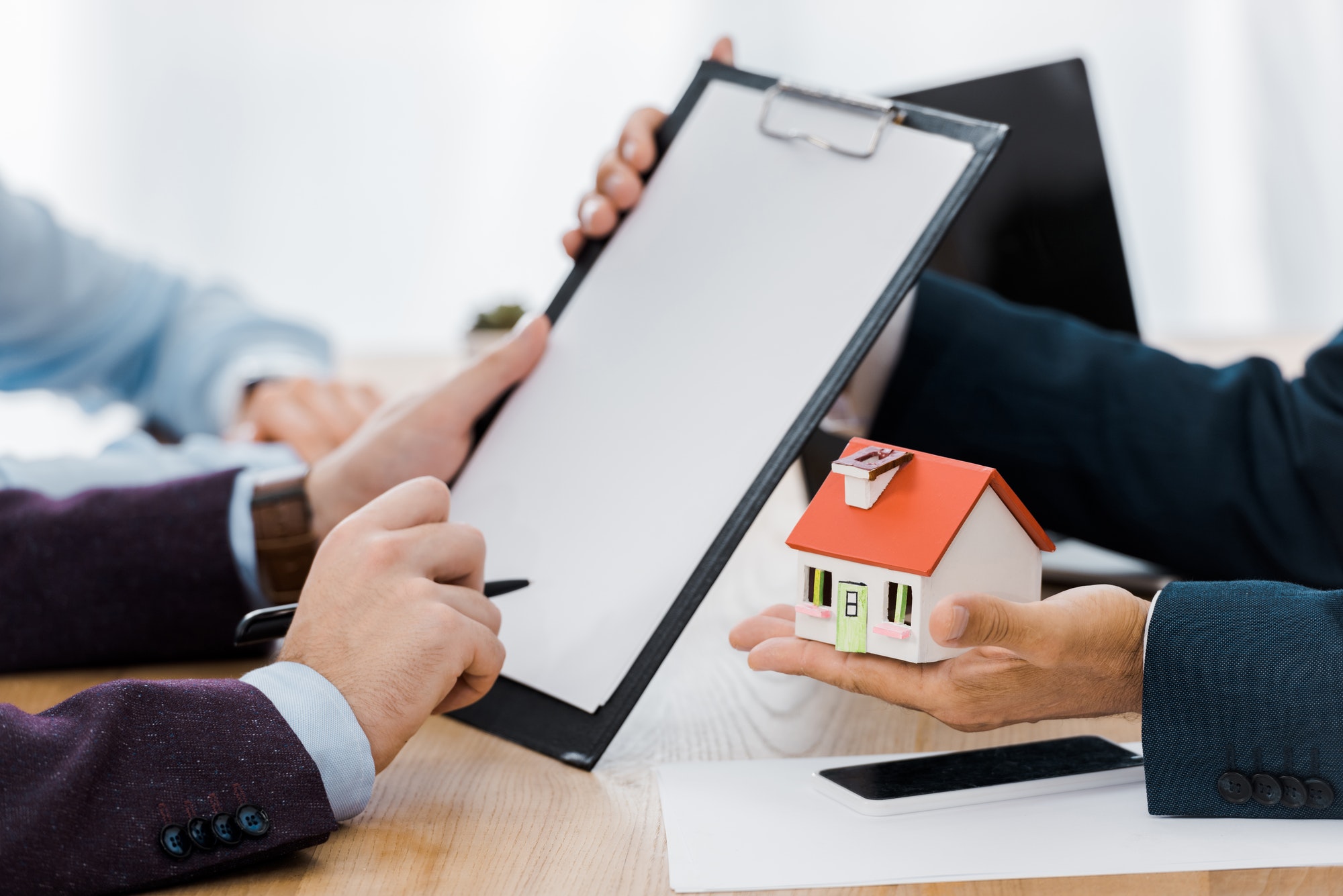 man signing contract on clipboard while insurance agent holding house model